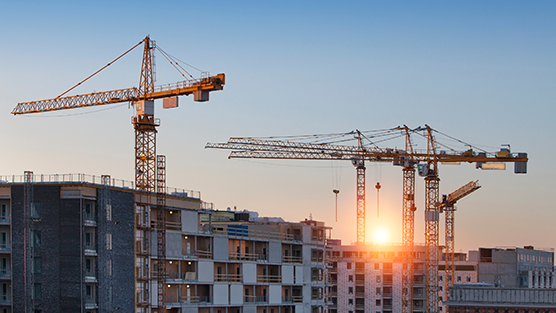 Nostureita rakennustyömaalla, jossa näkyy keskeneräisiä kerrostaloja auringonlaskua vasten.